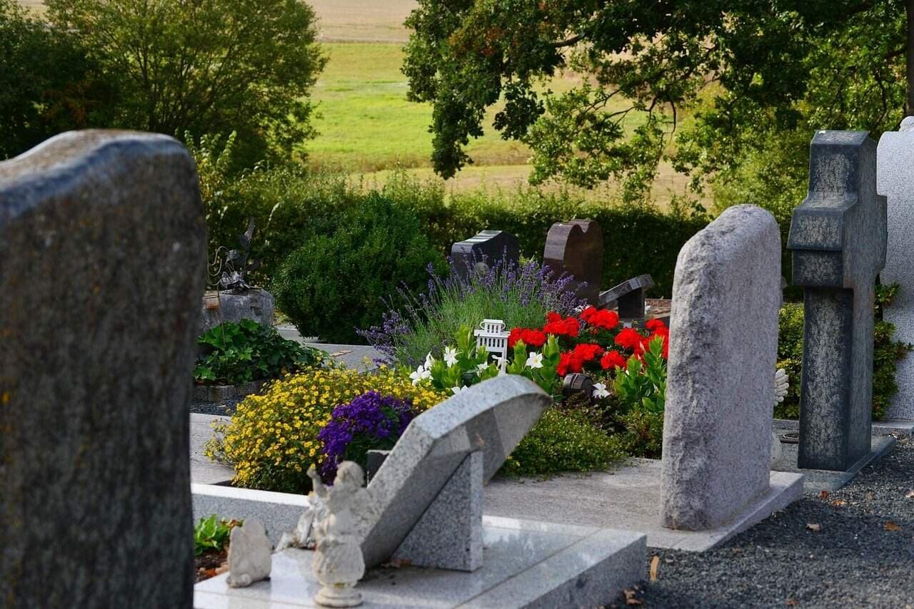Trauerredner Ostschweiz (Der Trauerengel) 7 Trauerengel auf einem Grab mit Blumen und Gräbern im Hintergrund.